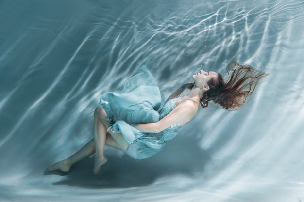 Jolie fille aux cheveux dénoués dans une robe bleue flottant sous l'eau.