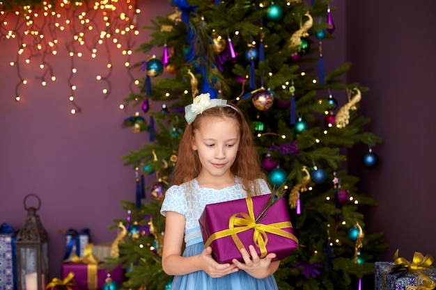 Jolie fille aux cheveux longs tenant une boîte-cadeau près de l'arbre de Noël