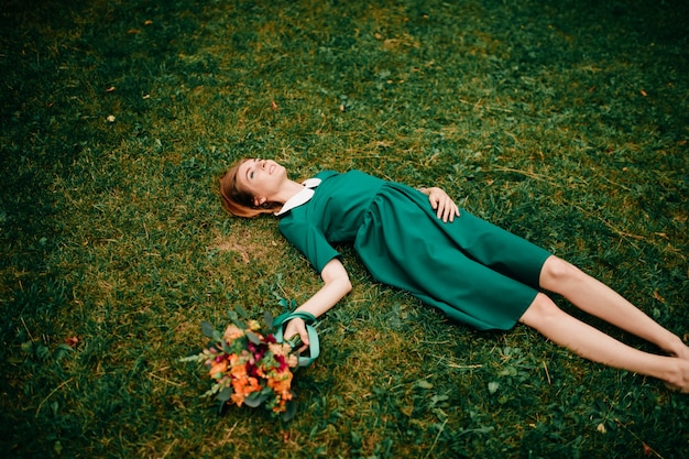 Jolie fille aux cheveux rouges en robe verte allongée sur l'herbe