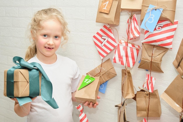 Une jolie fille aux dents de lait perdues se réjouit d'un cadeau de Noël sur fond de calendrier de l'avent