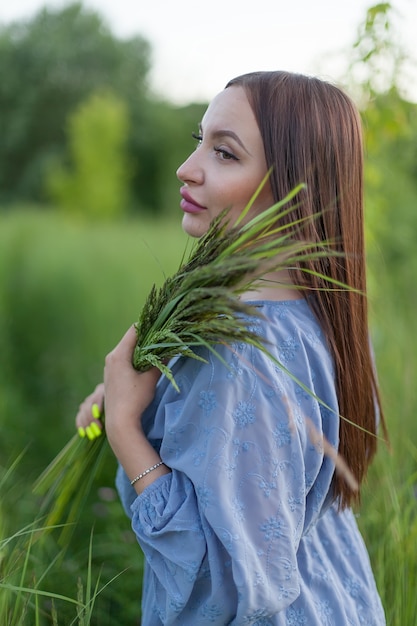Jolie fille aux longs cheveux noirs posant dans un champ de blé, tenant des épillets dans ses mains