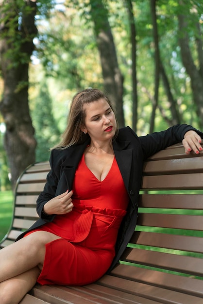 Jolie fille blonde sur un banc dans le parc Jeune femme en robe rouge se détend dans le parc le jour d'été Cadre vertical