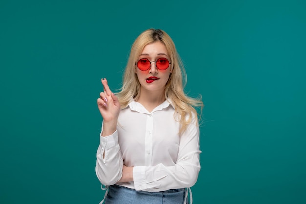 Jolie fille blonde belle jeune fille dans une chemise blanche soignée croisant les doigts en espérant