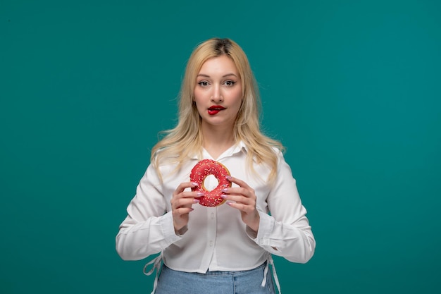 Jolie fille blonde belle jeune fille dans une chemise blanche soignée se mordant les lèvres pensant manger un beignet