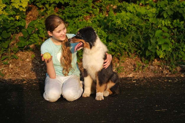 Jolie fille blonde caucasienne heureuse adolescente jouer avec un chien chiot berger australien trois couleurs en été avec ballon. Formation. Profitez du temps ensemble. Concept de soins pour animaux de compagnie. L'amour entre l'humain et l'animal.