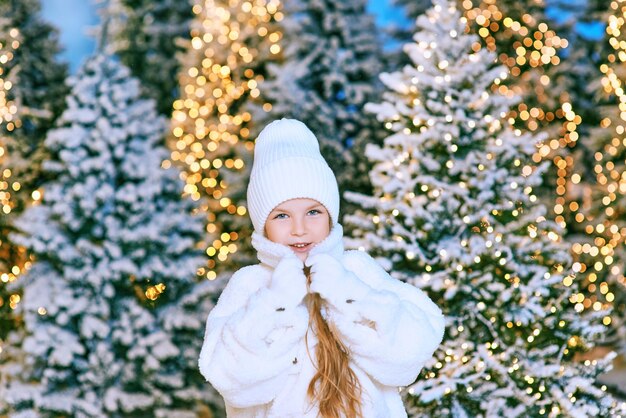 jolie fille blonde caucasienne en manteau de fourrure écologique blanc, chapeau et gants marchant en hiver noël