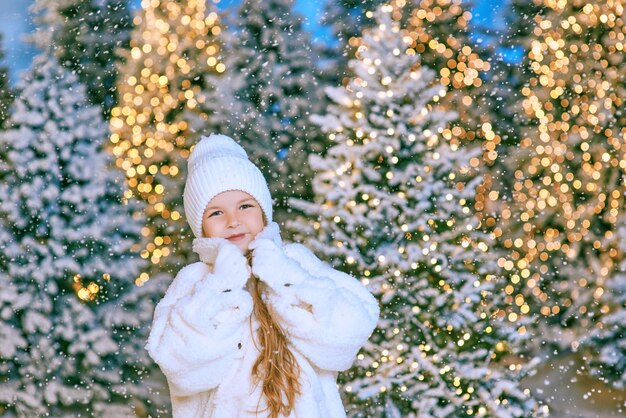 jolie fille blonde caucasienne en manteau de fourrure écologique blanc, chapeau et gants marchant en hiver noël