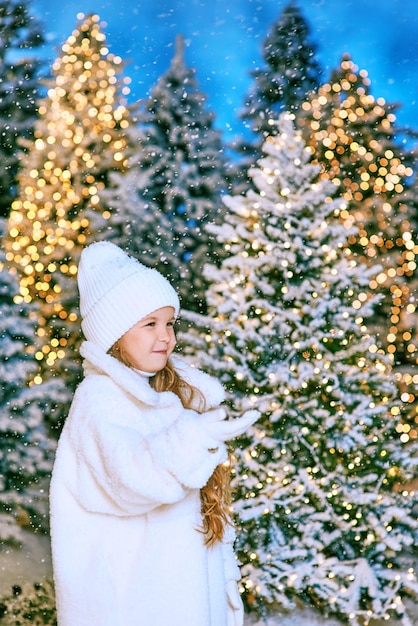 jolie fille blonde caucasienne en manteau de fourrure écologique blanc, chapeau et gants marchant en hiver noël