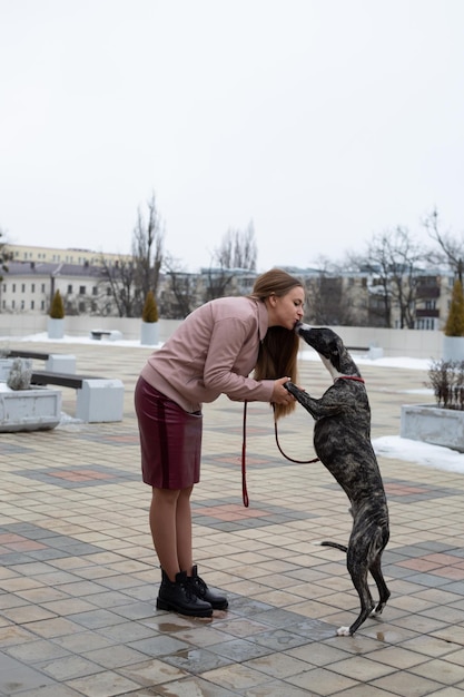 une jolie fille blonde est assise en train de former un chien whippet dans la rue de la ville