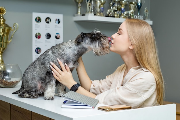 jolie fille blonde est debout à la réception où un chien Schnauzer miniature est assis