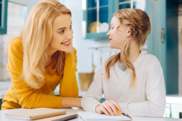 Jolie fille blonde joyeuse souriante et tenant un crayon pendant qu'elle et sa mère se regardent