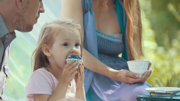 Jolie fille blonde mangeant un petit gâteau en plein air avec la famille, gros plan