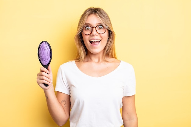 Jolie fille blonde à la recherche d'un concept de brosse à cheveux heureux et agréablement surpris