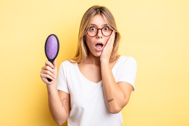 Jolie fille blonde se sentant choquée et effrayée. concept de brosse à cheveux