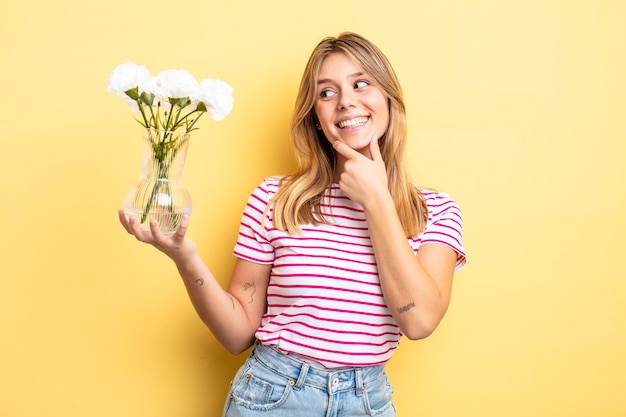 Jolie fille blonde souriante avec une expression heureuse et confiante avec la main sur le menton. concept de fleurs décoratives