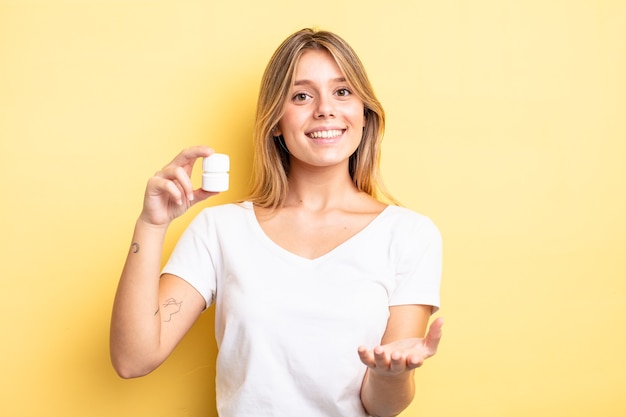 Jolie fille blonde souriante joyeusement avec amicale et offrant et montrant un concept. concept de bouteille de pilules