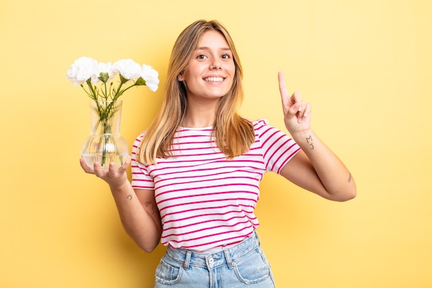 Jolie fille blonde souriante et semblant amicale, montrant le numéro un. concept de fleurs décoratives