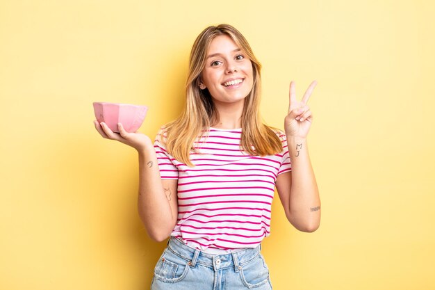 Jolie fille blonde souriante et sympathique, montrant le numéro deux. concept de bol vide