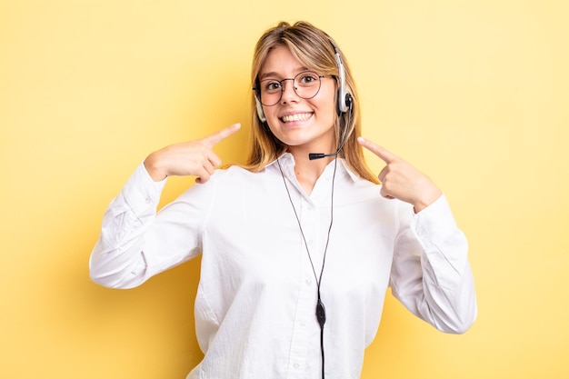 Jolie fille blonde souriante en toute confiance pointant vers son large sourire. notion de casque