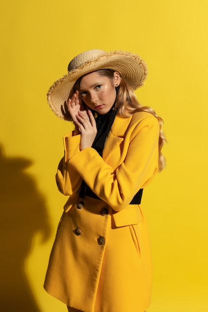 Jolie fille blonde avec des taches de rousseur en tenue jaune et chapeau de paille sur jaune