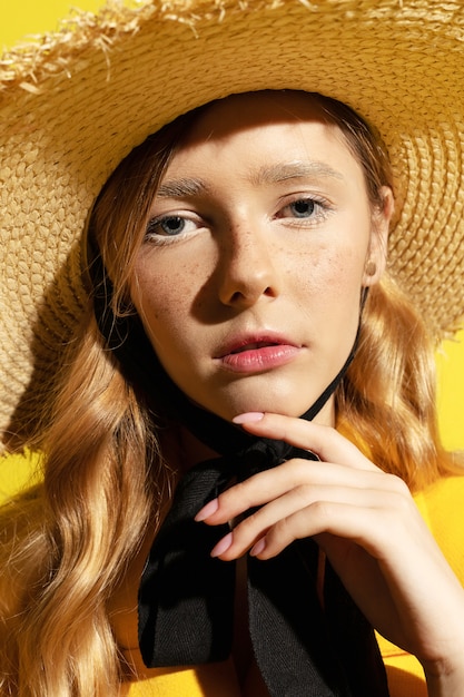 Jolie fille blonde avec des taches de rousseur en tenue jaune et chapeau de paille sur jaune