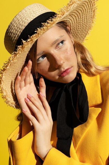 Photo jolie fille blonde avec des taches de rousseur en tenue jaune et chapeau de paille sur jaune