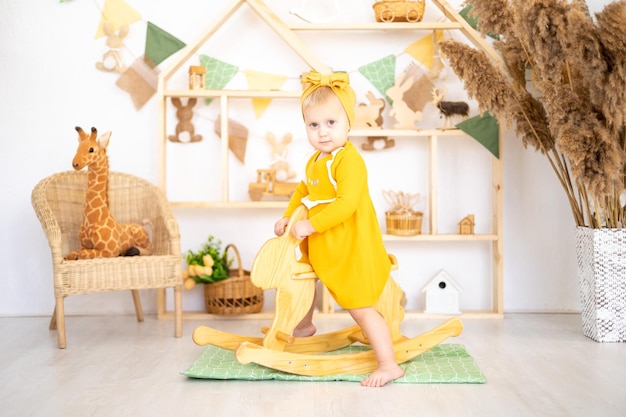 Jolie fille en bonne santé jouant avec des jouets éducatifs en bois dans une chambre d'enfants confortable et lumineuse à la maison dans le contexte d'une maison en bois assise sur un jouet à bascule en bois