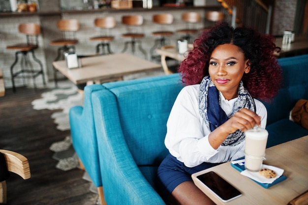 Jolie fille bouclée afro-américaine assise au café avec latte