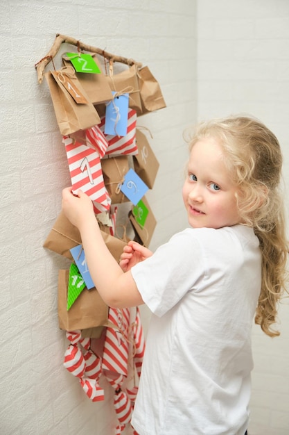 Jolie fille bouclée aux cheveux blonds et une fille et un calendrier de l'avent accroché au mur la veille de noël