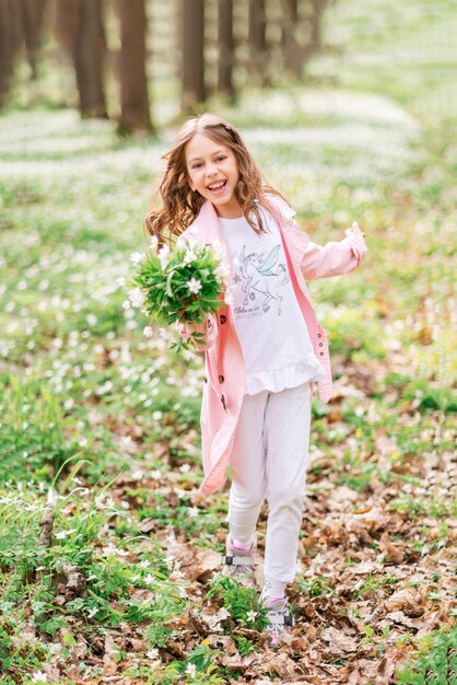 Jolie fille avec un bouquet de perce-neige se promène dans la forêt printanière. L'enfant sourit et se réjouit au printemps.