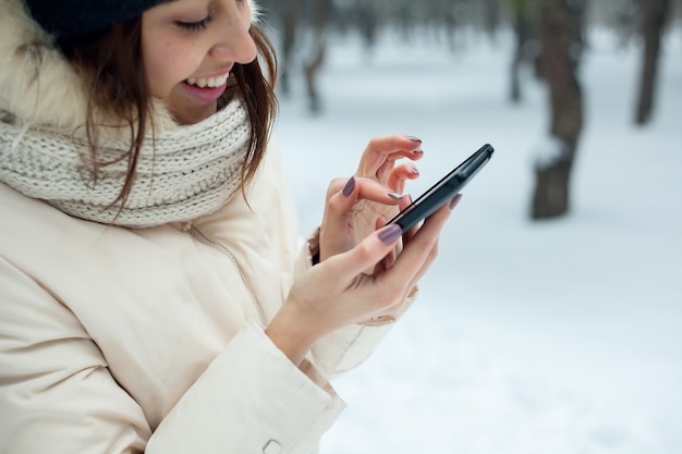 Jolie fille brune à l'aide de son smartphone sur la forêt enneigée