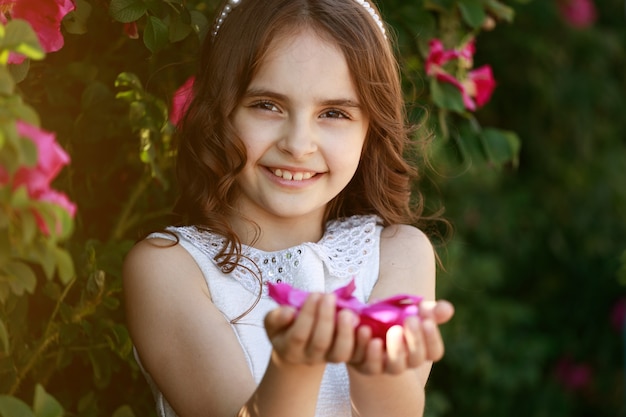 Jolie fille brune aux cheveux noirs sur fond de fleurs dans le parc. portrait d'enfant. photo de haute qualité