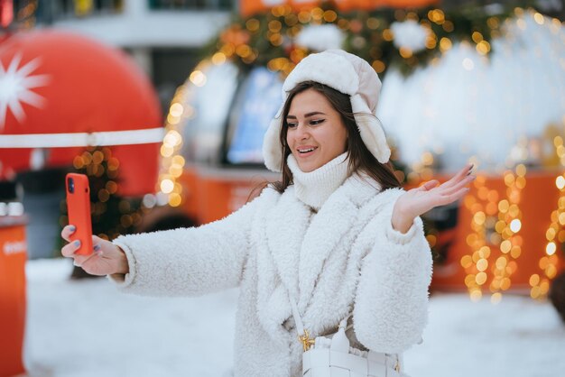 Jolie fille brune caucasienne en chapeau de fourrure d'hiver et manteau debout à l'aire de restauration extérieure à la patinoire