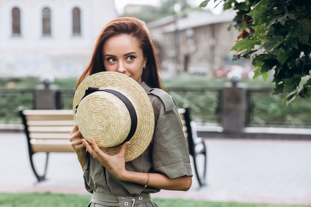 Jolie fille brune dans un chapeau de paille à l'extérieur, fille souriante se promène dans la ville en été