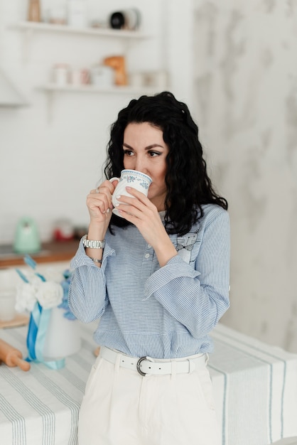 Jolie fille brune dans une chemise bleue boit dans une tasse