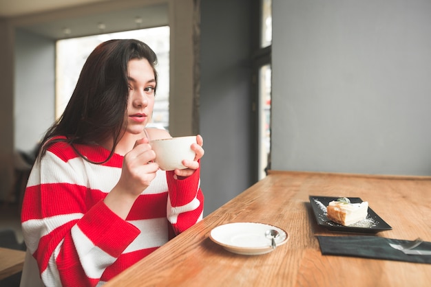 Jolie fille brune est assise dans un café avec une tasse de café