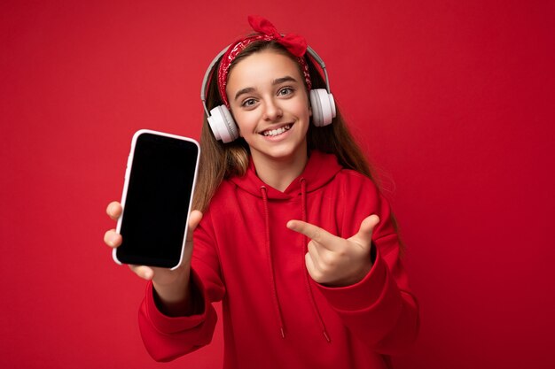 Jolie fille brune souriante positive portant un sweat à capuche rouge isolé sur fond rouge