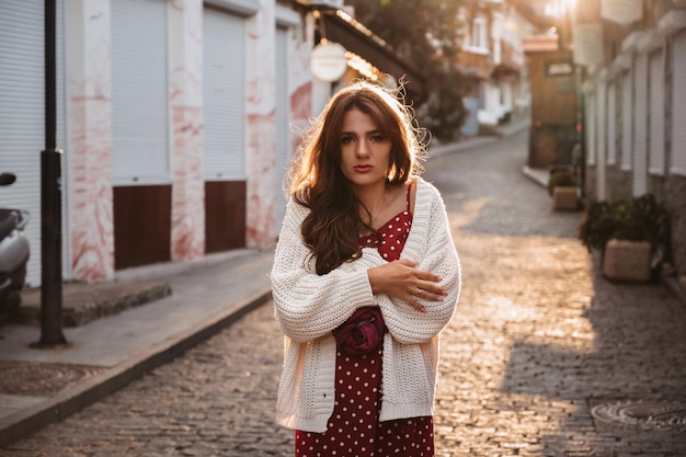 Jolie fille brune triste se réchauffe dans la rue enveloppée dans un pull