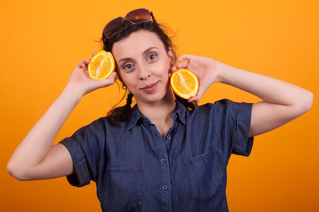 Jolie fille caucasienne tenant une orange en tranches et regardant la caméra sur fond jaune. Fille joyeuse avec des oranges juteuses.