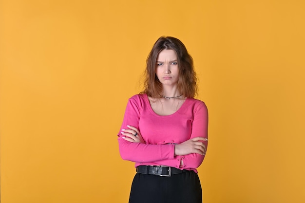 Jolie fille caucasienne triste se dresse sur un fond jaune dans un pull rose avec les mains jointes