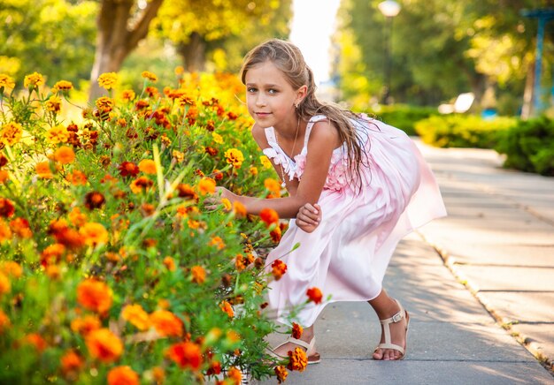 Une jolie fille charmante dans une belle robe rose renifle des soucis enflammés dans un parc lumineux par une journée ensoleillée lors de vacances tant attendues