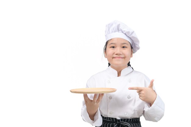 Jolie fille chef tient une assiette en bois et pointe son doigt sur une assiette isolée sur fond blanc. concept de présentation de menu alimentaire
