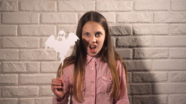 Jolie fille en chemisier rose tenant une bannière avec un fantôme blanc sur fond de mur de briques blanches