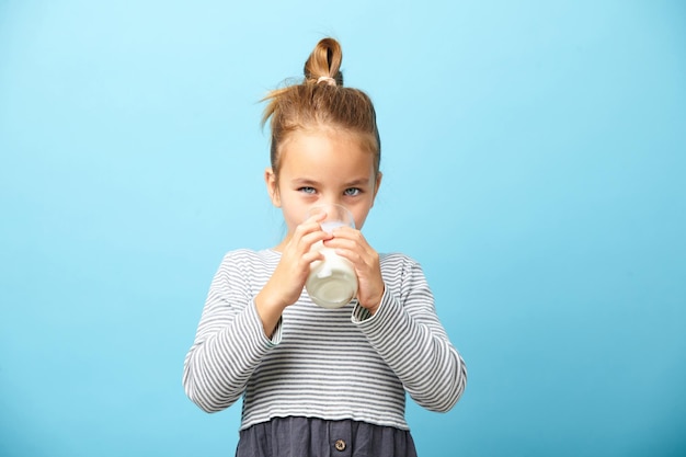 Jolie fille de cinq ans boit du lait sur bleu isolé