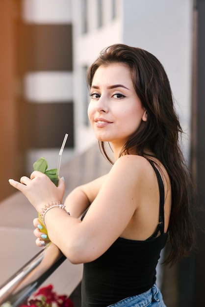 Jolie fille avec un cocktail jaune relaxant sur le balcon avec une belle vue