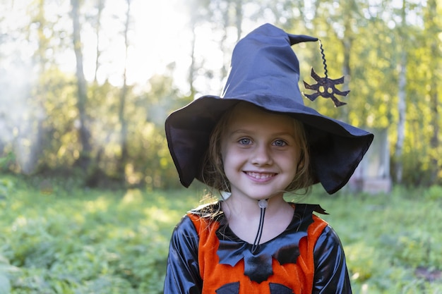 Jolie fille en costume de carnaval orange de sorcière pour les vacances d'halloween se tient parmi les arbres dans