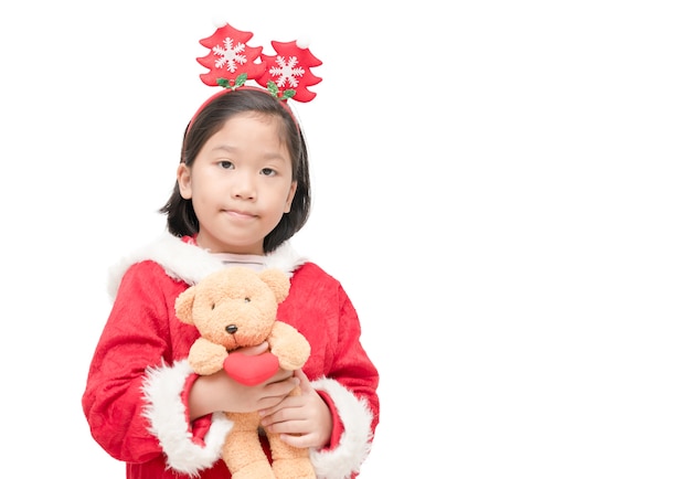 Jolie fille en costume de père Noël avec poupée ours en peluche et sourire isolé sur fond blanc, Noël