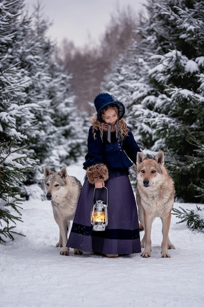 Une jolie fille dans un beau costume vintage se promène avec des loups dans la forêt d'hiver