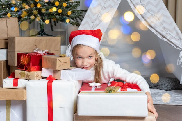 Une jolie fille dans un bonnet de Noel tient ses cadeaux pour le Nouvel An de Noël couché dans une chambre d'enfants décorée de guirlandes