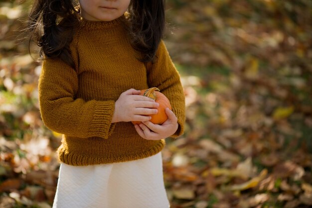 Une jolie fille dans un chandail tient une petite citrouille dans sa main